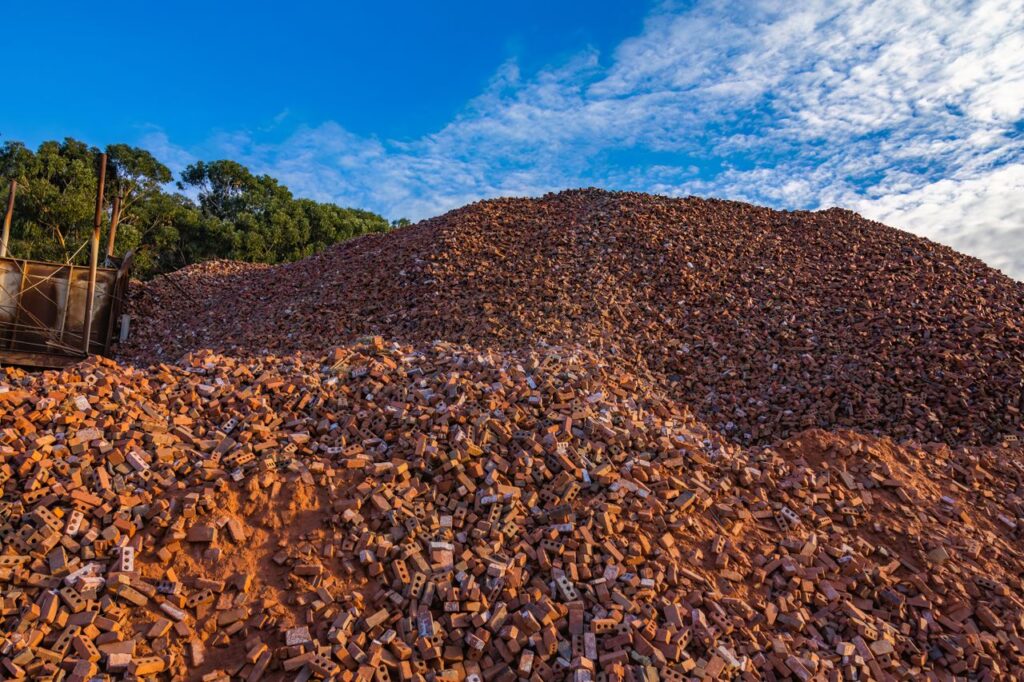 A large pile of bricks stacked outdoors under a clear blue sky, with trees in the background.